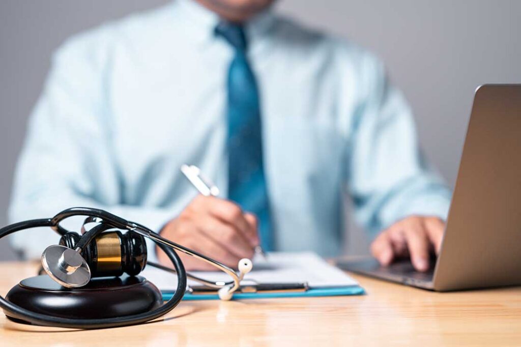 A person seated at a desk showing documents to a professional while discussing paperwork.